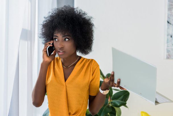 freelance afroamericano con cartellina che parla su smartphone a casa
 - Foto, immagini
