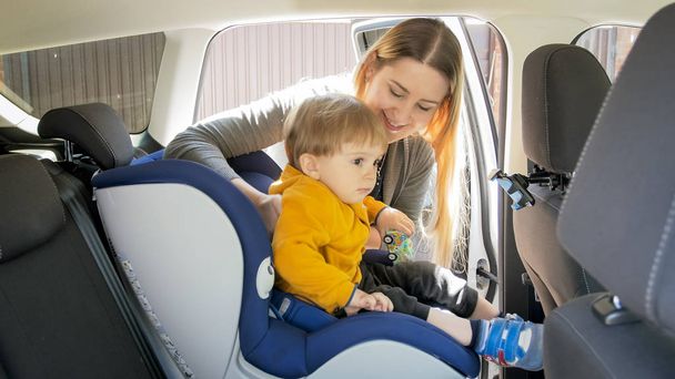 Muotokuva hymyilevä äiti istuu hänen lapsi poikansa auton turvaistuin
 - Valokuva, kuva