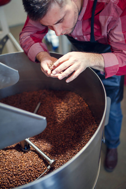 Picture of young businessman with coffee beans in hand next to roaster - Foto, imagen