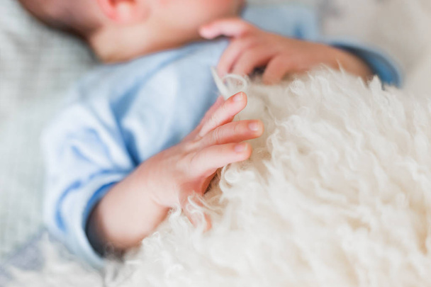Mano de palma de niño recién nacido. Dedos pequeños con uñas. Colcha de piel de oveja natural
. - Foto, Imagen