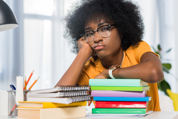 fatigué afro-américain freelance dans les lunettes appuyé sur pile de cahiers sur le lieu de travail au bureau à domicile
 - Photo, image