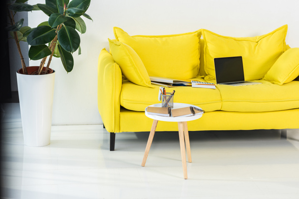 Nahaufnahme von Laptop, Notebooks und Ordnern auf gelbem Sofa im Home Office - Foto, Bild