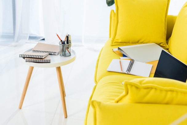 κλείνω πάνω θέα του lap-top, σημειωματάρια και τους φακέλους στον κίτρινο καναπέ στο σπίτι γραφείο - Φωτογραφία, εικόνα