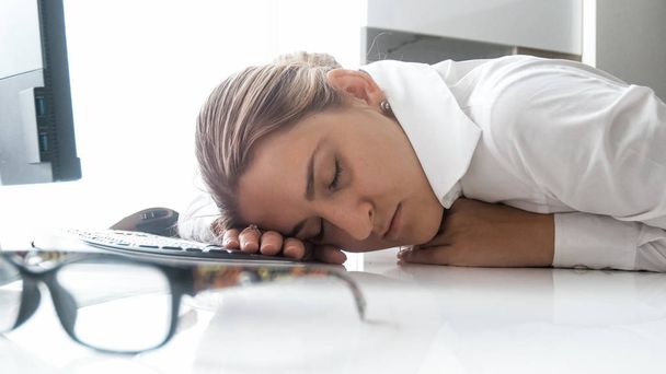 Retrato de la joven mujer de negocios agotada durmiendo en el escritorio en la oficina
 - Foto, imagen
