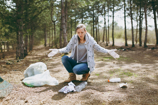 Geschokt jongedame in casual kleding en handschoenen rubbis schoonmaken - Foto, afbeelding