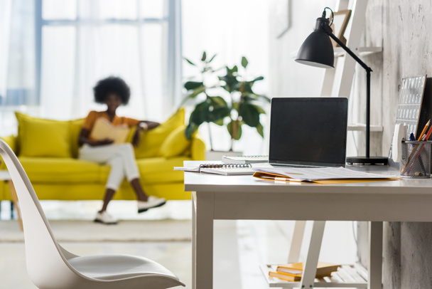 enfoque selectivo de la computadora portátil en la mesa y el freelancer afroamericano en la oficina en casa
 - Foto, imagen