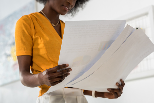 Plan recadré de belle pigiste afro-américaine avec des papiers dans les mains au bureau à la maison
 - Photo, image