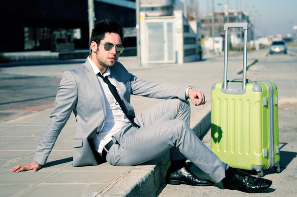 Man dressed in suit and suitcase sitting on the floor in the str - Photo, image
