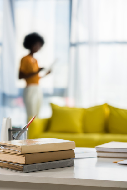 Selektivní fokus knih na pracovišti a africký Američan na pozadí v domácí kanceláři - Fotografie, Obrázek