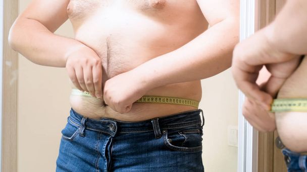 Mladý muž, měření tuku břicho s krejčovským metrem s nadváhou - Fotografie, Obrázek