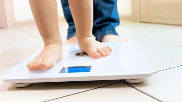Closeup image of babys feet standing on digital weight scales - Photo, Image