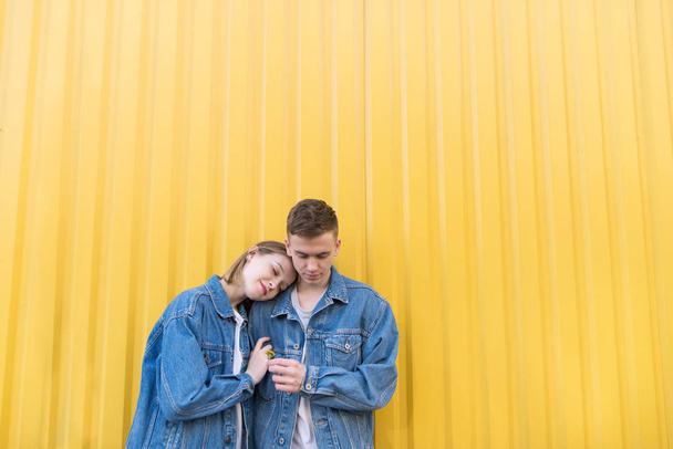 Красивая пара стоит на фоне желтой стены и обнимается. Симпатичные хипстеры в джинсовых куртках висят на желтом фоне
 - Фото, изображение