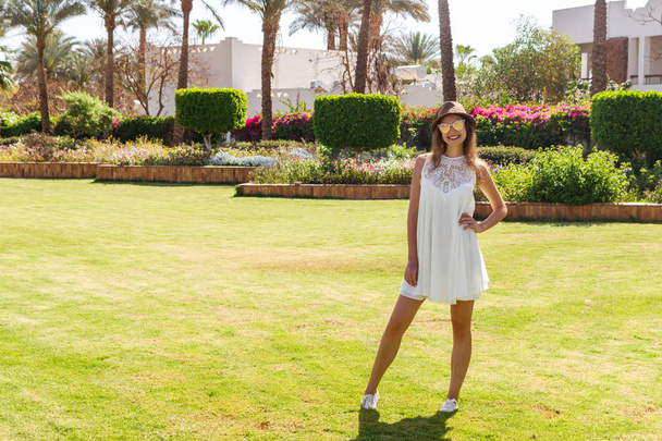 Όμορφη χαμογελαστή νεαρή κοπέλα με λευκό φόρεμα και καπέλο το καλοκαίρι - Φωτογραφία, εικόνα