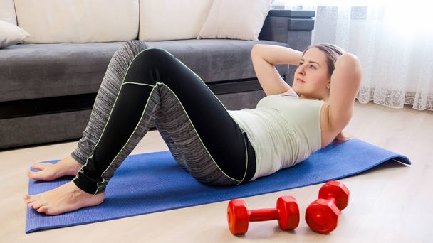 Young woman doing physical exercises on fitness mat at home - Photo, Image