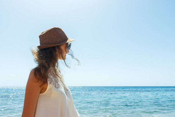 Jeune femme en chapeau debout sur une plage et regardant vers un horizon de mer
 - Photo, image