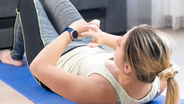 Молодая женщина лежит на коврике фитнес и использовать фитнес умные часы
 - Фото, изображение