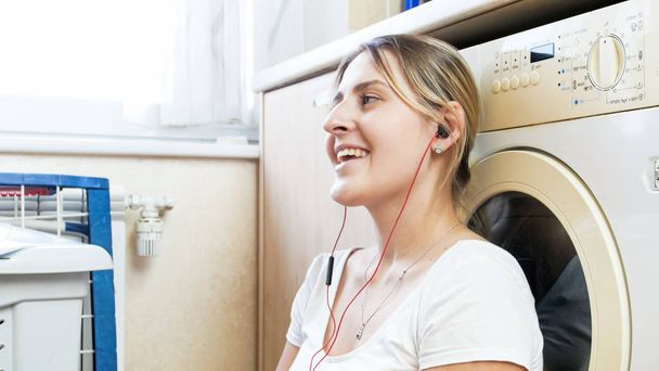 Happy usmívající se hospodyně s sluchátka zpívá při čekání na prádlo - Fotografie, Obrázek