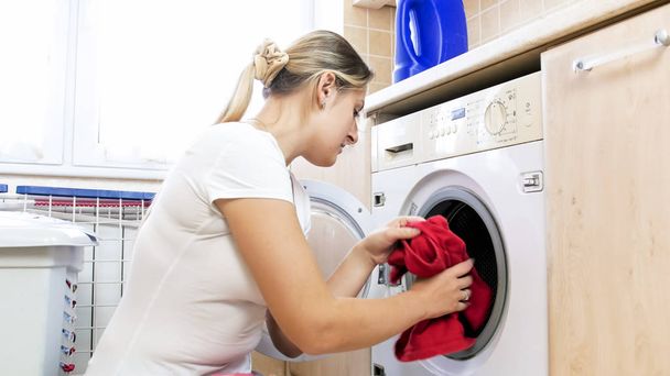 Portrait of young housewife takes red towel out of washing machine - Zdjęcie, obraz