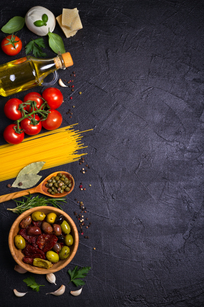 Selection of healthy food. Italian food background with spaghetti, mozzarella parmesan cheese, olives, tomatoes and rosemary. Vegetarian food banner. overhead, vertical - Photo, Image