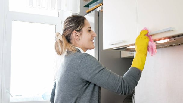 Portrait of young smiling woman washing cupboard and cabinets on kitchen - Photo, Image