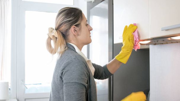Portrait of young blonde woman washing cupboards on kitchen with cloth - Foto, Bild