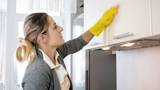 Portrait of beautiful young housewife washing cupboards with cloth - Foto, Imagem