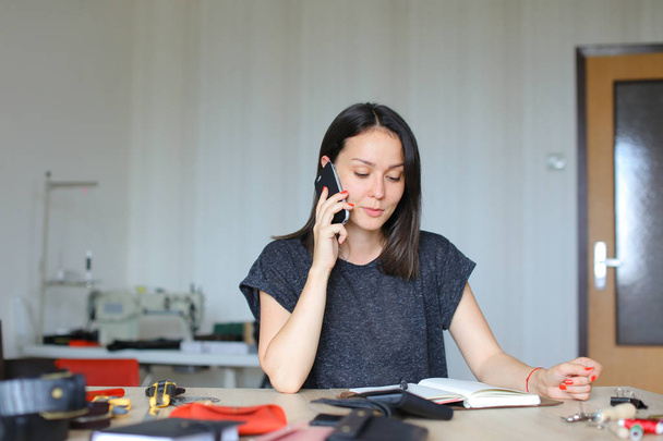 Persona femminile seduta in atelier di pelle e fare notebook e portafogli fatti a mano, parlando con lo smartphone
 - Foto, immagini