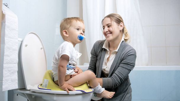 Портрет щасливої усміхненої молодої матері зі своїм маленьким хлопчиком в туалеті
 - Фото, зображення