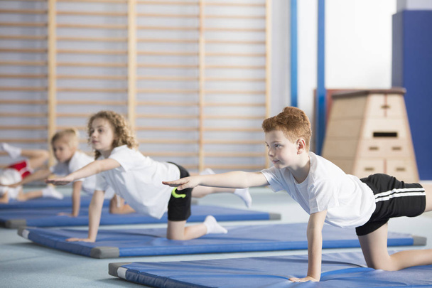 Group of children doing gymnastics on blue mats during physical education class at school - Fotó, kép