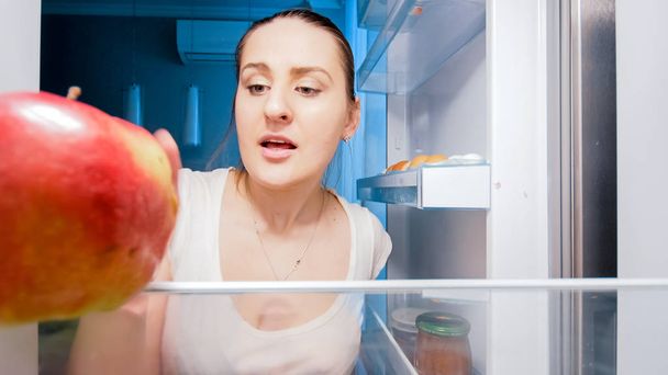 Closeup image of young hungry woman looking for something to eat in refrigerator at night - 写真・画像