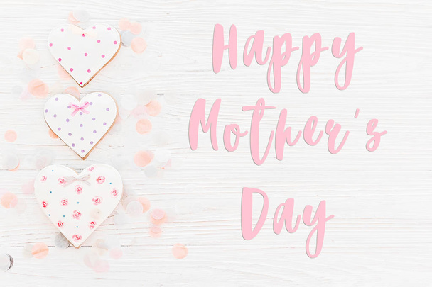 view of happy mothers day text with pink cookies hearts on white rustic wooden background with confetti in soft light. - Photo, Image