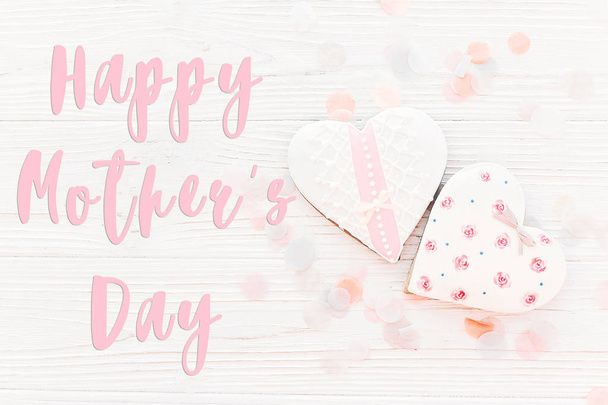 glückliche Muttertagstext mit rosa Plätzchen Herzen auf weißem rustikalem Holzhintergrund mit Konfetti in weichem Licht. - Foto, Bild