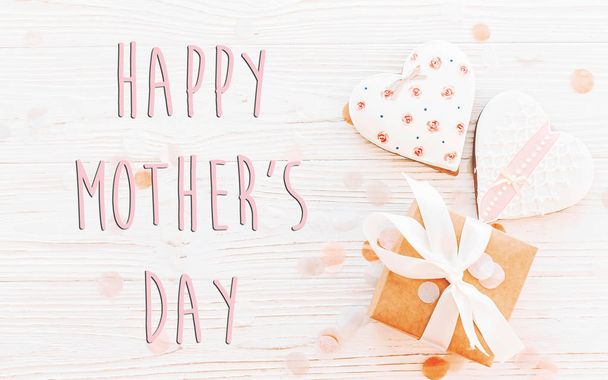 ευτυχισμένος μητέρες ημέρα κείμενο με ροζ μπισκότα καρδιές με το κιβώτιο δώρων σε άσπρο φόντο ρουστίκ ξύλινα - Φωτογραφία, εικόνα