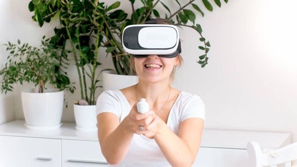 Portrait of laughing young woman playing video games in VR helmet - Photo, Image
