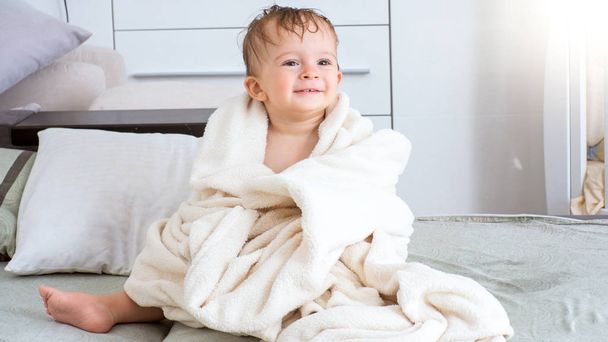 Портрет милого улыбающегося мальчика, сидящего под полотенцем после ванны
 - Фото, изображение