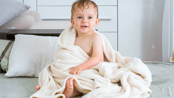 Ritratto di bambino di 1 anno coperto di asciugamano bianco seduto sul letto
 - Foto, immagini