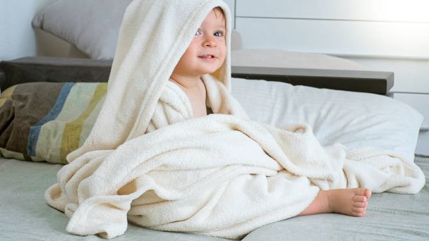 Portrait de mignon garçon tout-petit de 1 an assis sous une grande serviette après avoir pris un bain
 - Photo, image