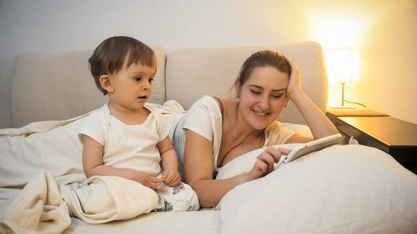 Adorable toddler boy watching as his mother using digital tablet in bed - Zdjęcie, obraz