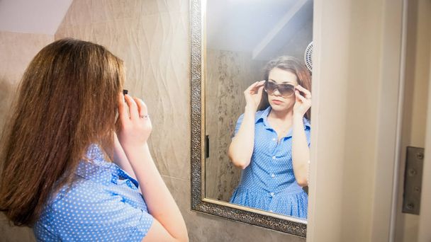 Portrait de jeune femme essayant des lunettes de soleil devant le miroir à la salle de bain
 - Photo, image