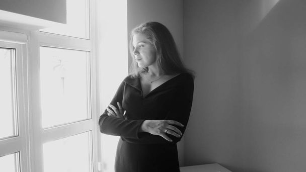 Immagine in bianco e nero di giovane donna elegante che guarda fuori da una grande finestra
 - Foto, immagini