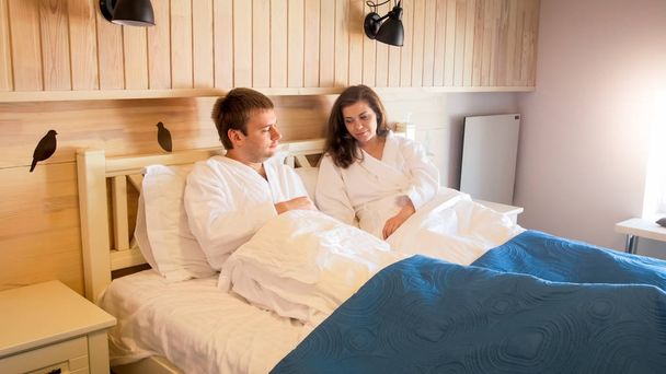 Happy young couple in bathrobes lying in bed at morning - Foto, imagen