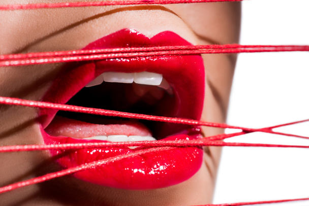 cropped image of woman with red lipstick and open mouth touching red threads isolated on white - Foto, imagen