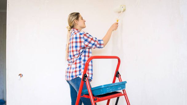 Πορτρέτο του όμορφη νεαρή γυναίκα βαφή τοίχων στο νέο σπίτι της - Φωτογραφία, εικόνα