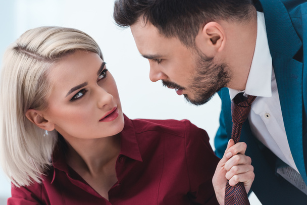 young business people looking at each other while businesswoman holding necktie of handsome businessman - Photo, Image