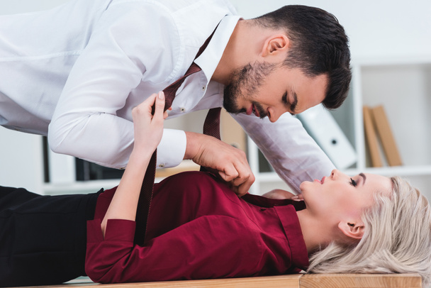 side view of businessman unbuttoning shirt of young businesswoman at workplace - Foto, Bild
