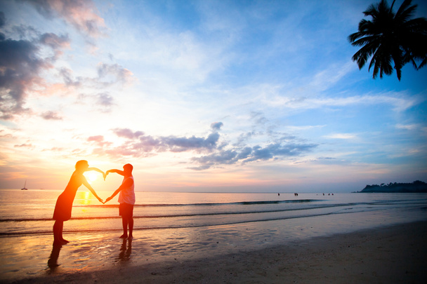 Jeune couple tenant la main en forme de coeur sur la plage de la mer au coucher du soleil
. - Photo, image