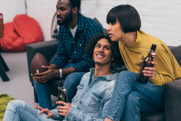 group of young multiethnic friends with bottles of beer watching american football match  - Photo, Image