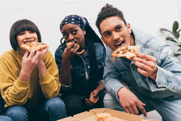 Lächelnde multikulturelle Gruppe von Freunden, die Pizza essen und sich das Spiel ansehen - Foto, Bild