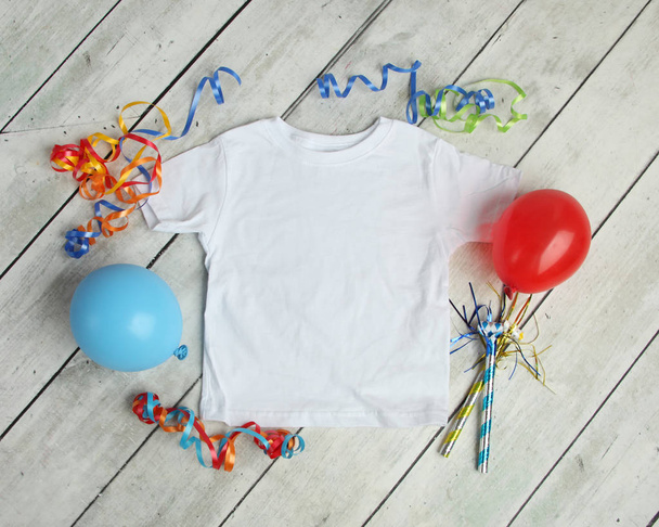 Plat lag mockup van witte kinder kinderen t shirt voor verjaardagsviering met ballonnen, slingers en decoratie - Foto, afbeelding