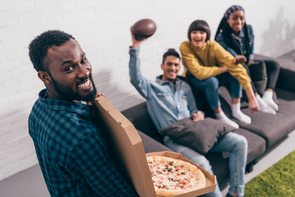 high angle view of young black man with pizza box and friends on couch behind - Foto, Imagem